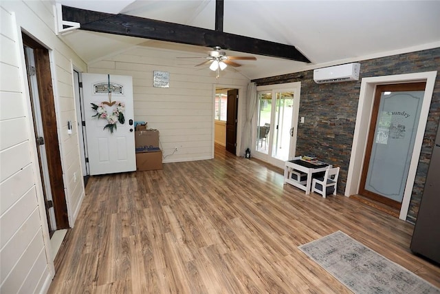 unfurnished living room with an AC wall unit, vaulted ceiling with beams, ceiling fan, and hardwood / wood-style floors