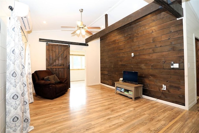 living room with wooden walls, vaulted ceiling, ceiling fan, a barn door, and light hardwood / wood-style floors