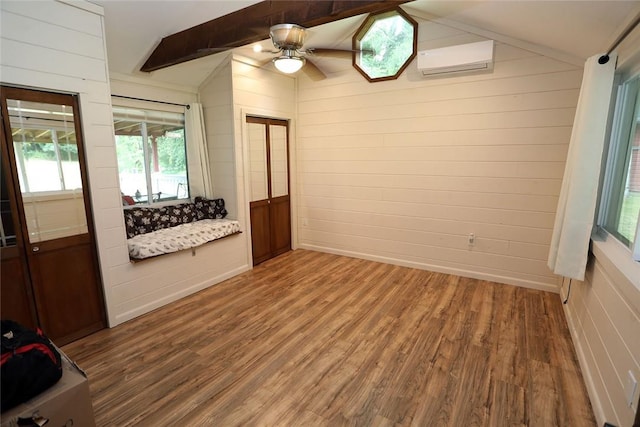 spare room with lofted ceiling with beams, hardwood / wood-style flooring, a wall unit AC, and plenty of natural light