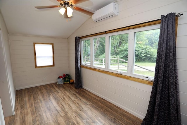 empty room with a wall mounted air conditioner, wood-type flooring, vaulted ceiling, and plenty of natural light