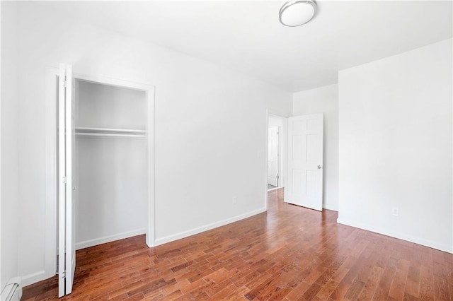 unfurnished bedroom featuring a closet, wood-type flooring, and a baseboard heating unit