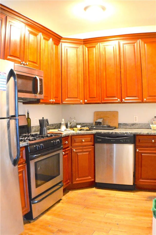 kitchen with light stone countertops, stainless steel appliances, and light wood-type flooring