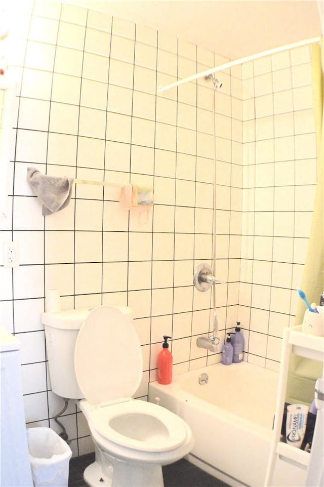 bathroom featuring tiled shower / bath combo, toilet, and tile walls