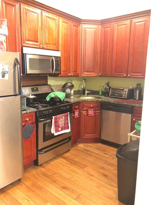 kitchen with dark stone countertops, sink, light wood-type flooring, and stainless steel appliances