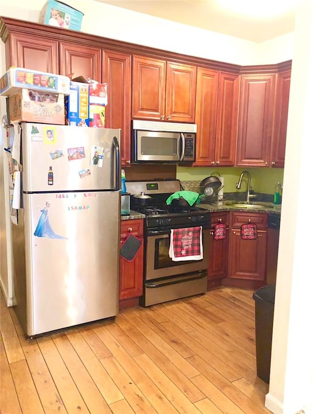 kitchen featuring dark stone countertops, light wood-type flooring, sink, and appliances with stainless steel finishes