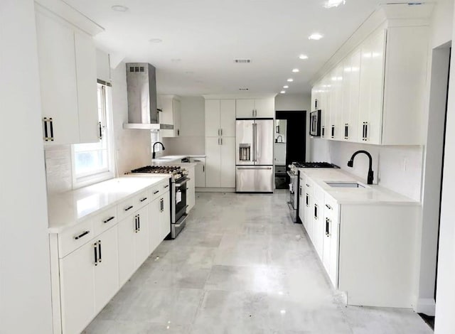 kitchen with appliances with stainless steel finishes, white cabinetry, wall chimney exhaust hood, and sink