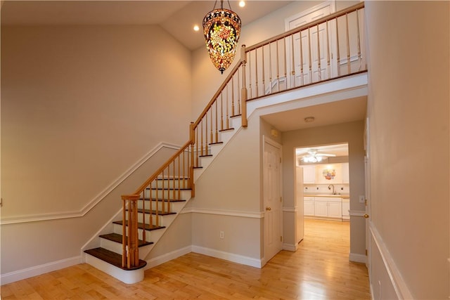 staircase with wood-type flooring, high vaulted ceiling, and sink