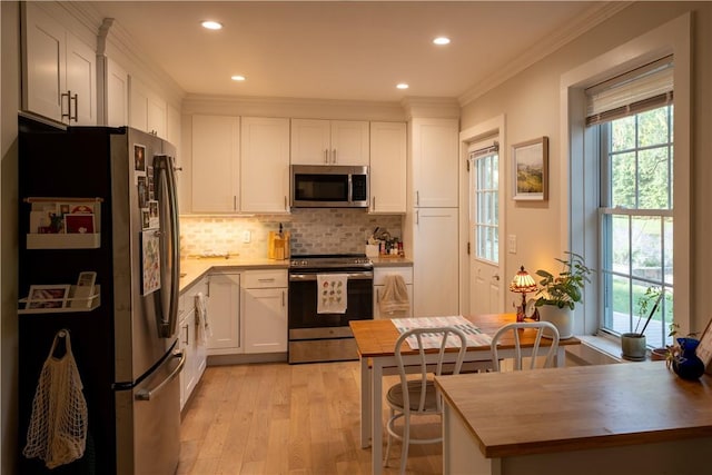 kitchen featuring backsplash, light wood-type flooring, ornamental molding, appliances with stainless steel finishes, and white cabinetry