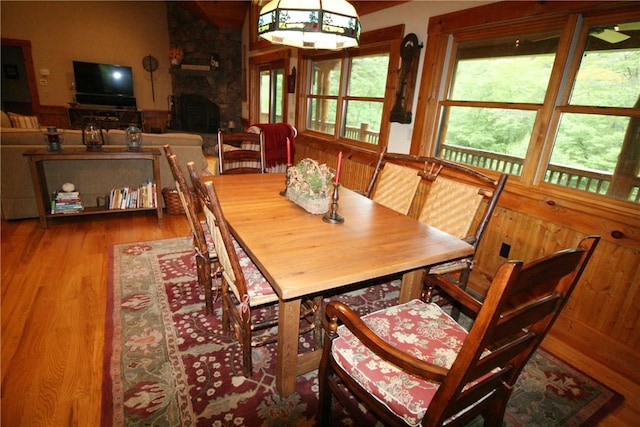 dining area with hardwood / wood-style floors, a stone fireplace, and wooden walls