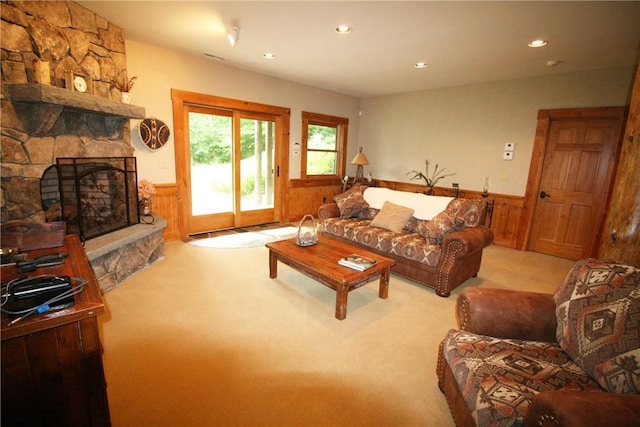 carpeted living room featuring a stone fireplace and wooden walls