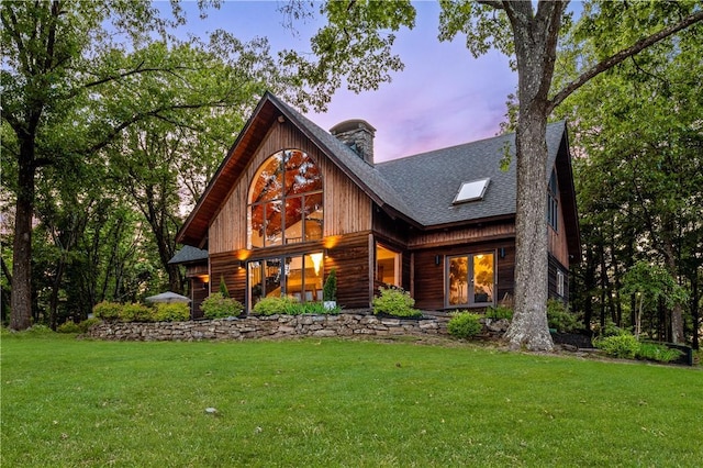 view of front of property featuring a shingled roof, a chimney, and a yard