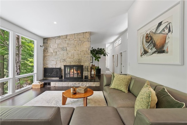 living room featuring hardwood / wood-style floors, vaulted ceiling, and a stone fireplace