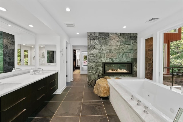 bathroom with tile patterned flooring, vanity, tiled tub, and a wealth of natural light