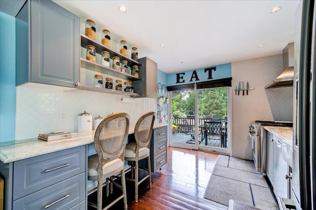 kitchen with wall chimney range hood, electric range, dark hardwood / wood-style floors, light stone counters, and a breakfast bar area