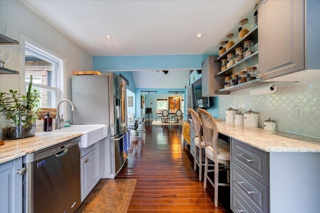 kitchen featuring gray cabinetry, dishwasher, backsplash, dark wood-type flooring, and light stone countertops