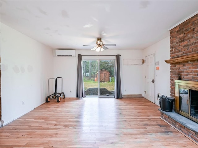 unfurnished living room featuring a wall mounted AC, ceiling fan, light wood-type flooring, and a brick fireplace