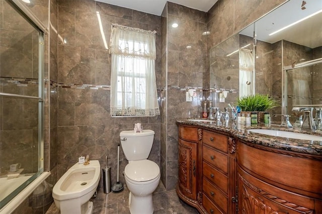 full bathroom featuring a bidet, bath / shower combo with glass door, toilet, vanity, and tile walls