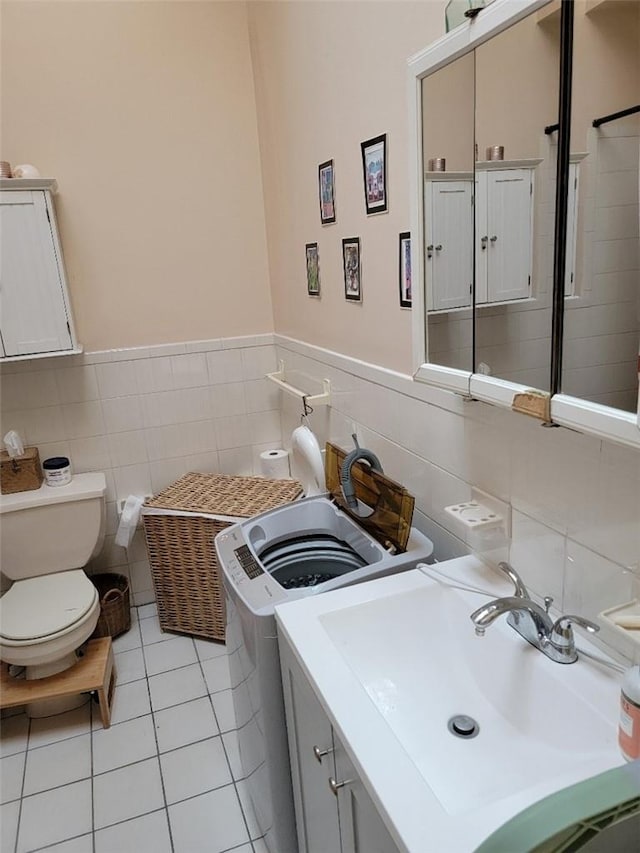 bathroom with tile patterned floors, sink, toilet, separate washer and dryer, and tile walls