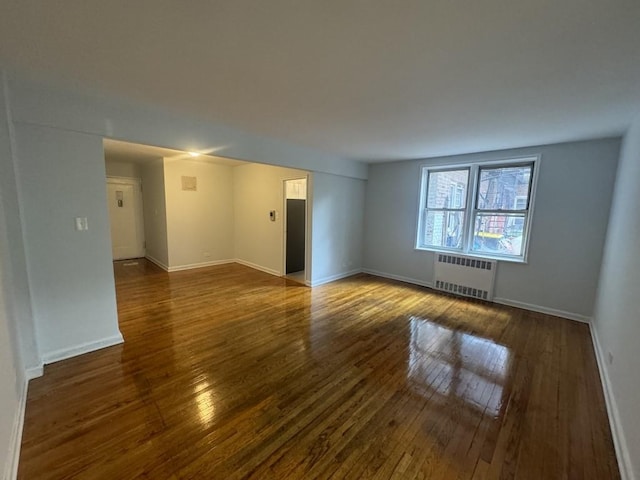 empty room with dark hardwood / wood-style flooring and radiator heating unit