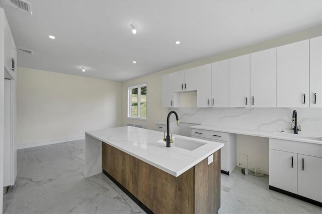 kitchen with a kitchen island with sink, sink, and white cabinets