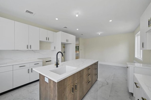 kitchen featuring sink, tasteful backsplash, white cabinetry, and an island with sink