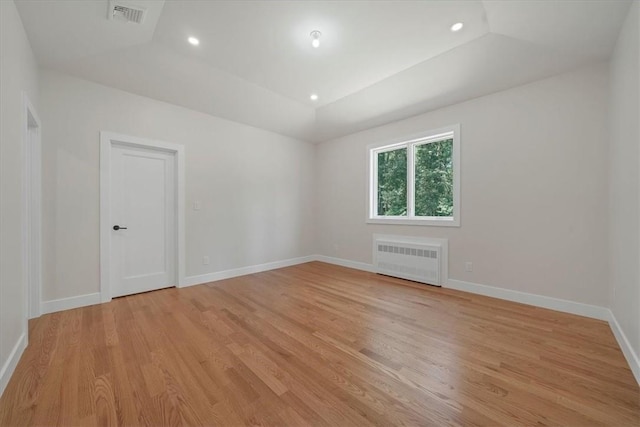 spare room with light wood-type flooring, a tray ceiling, and radiator