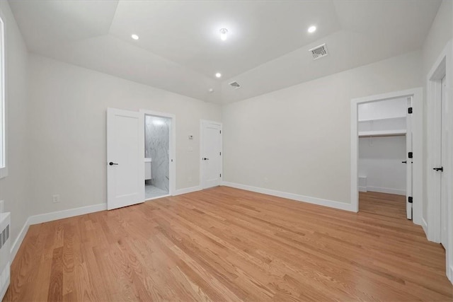 unfurnished bedroom featuring light wood-type flooring, ensuite bath, vaulted ceiling, a spacious closet, and a closet