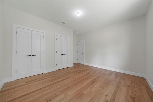 unfurnished bedroom with light hardwood / wood-style floors and multiple closets