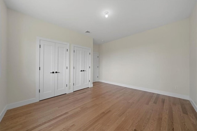 unfurnished bedroom with multiple closets and light hardwood / wood-style flooring