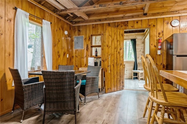 dining area with beamed ceiling, light wood-type flooring, and wood walls