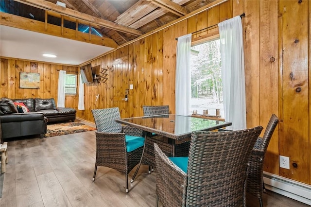 dining room featuring vaulted ceiling with beams, a wealth of natural light, wooden walls, and a baseboard radiator