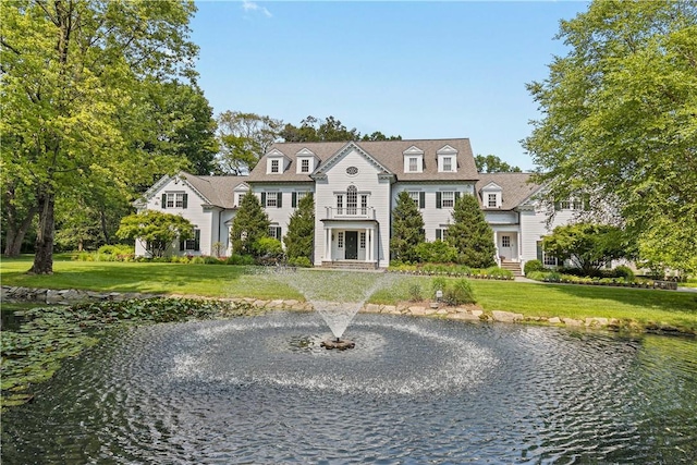 view of front of home featuring a front lawn, a balcony, and a water view