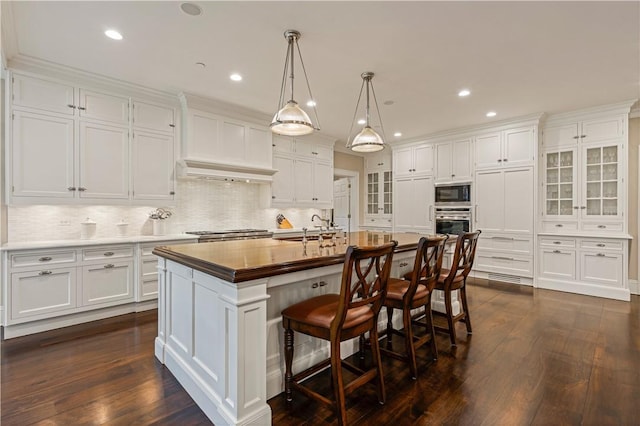 kitchen featuring white cabinets, black microwave, dark hardwood / wood-style flooring, and an island with sink