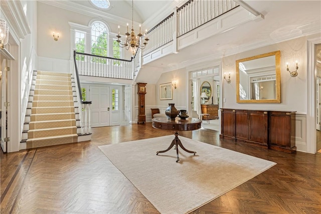 foyer entrance with a notable chandelier, dark parquet floors, ornamental molding, and a high ceiling