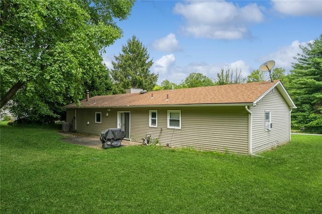 rear view of property featuring a patio, a chimney, a shingled roof, a lawn, and central AC