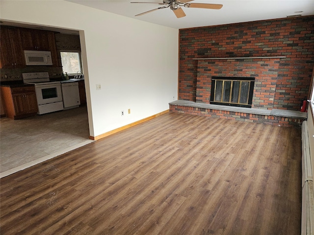 unfurnished living room with baseboards, ceiling fan, wood finished floors, a brick fireplace, and a sink