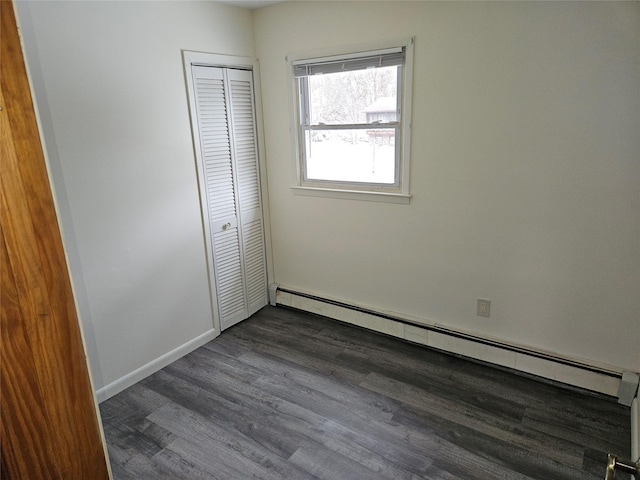 unfurnished bedroom with dark wood-style floors, a baseboard radiator, a closet, and baseboards