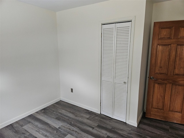 unfurnished bedroom with a closet, dark wood finished floors, and baseboards