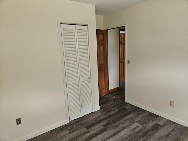 unfurnished bedroom featuring a closet, dark wood finished floors, and baseboards