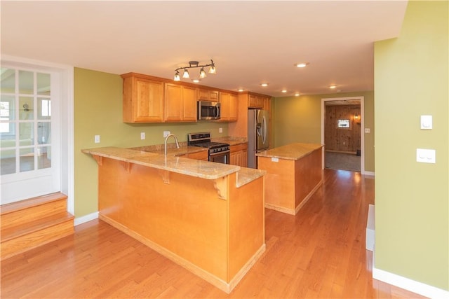 kitchen with a kitchen bar, kitchen peninsula, light hardwood / wood-style flooring, and stainless steel appliances