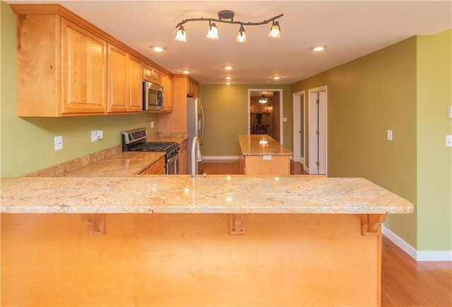 kitchen featuring a kitchen breakfast bar, appliances with stainless steel finishes, light hardwood / wood-style floors, light stone counters, and kitchen peninsula