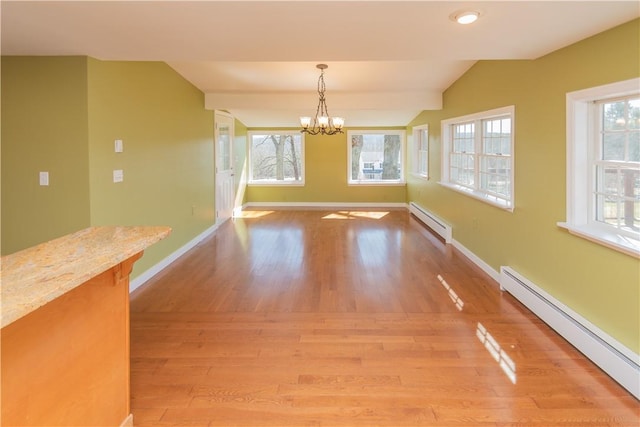 unfurnished dining area with a notable chandelier, vaulted ceiling, wood-type flooring, and a baseboard heating unit