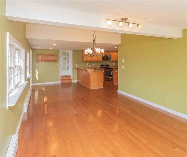 kitchen with appliances with stainless steel finishes, light wood-type flooring, pendant lighting, a notable chandelier, and a breakfast bar area