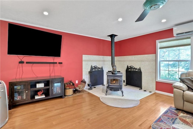 living room with a wood stove, ceiling fan, an AC wall unit, hardwood / wood-style floors, and ornamental molding