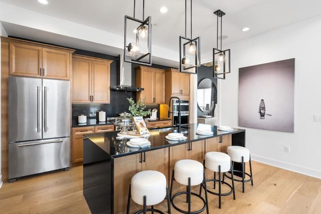 kitchen featuring stainless steel fridge, an island with sink, light hardwood / wood-style floors, and wall chimney range hood