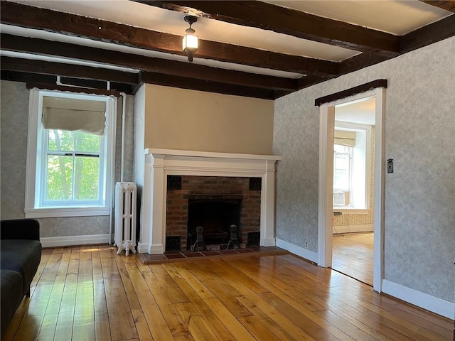 unfurnished living room featuring a brick fireplace, cooling unit, wood-type flooring, beamed ceiling, and radiator heating unit