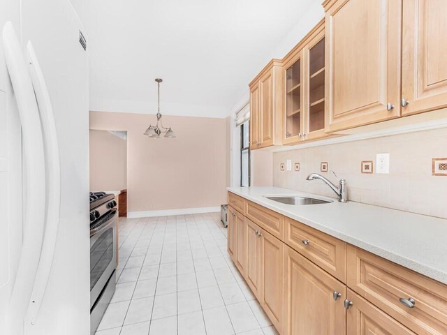 kitchen featuring sink, stainless steel gas range, light tile patterned floors, decorative light fixtures, and white fridge