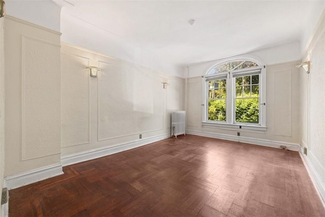 spare room featuring dark parquet flooring and radiator heating unit