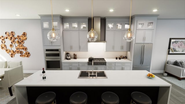 kitchen featuring a large island with sink, appliances with stainless steel finishes, sink, and wall chimney range hood