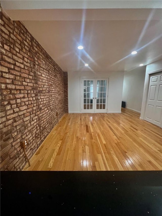 unfurnished room with french doors, light hardwood / wood-style flooring, and brick wall